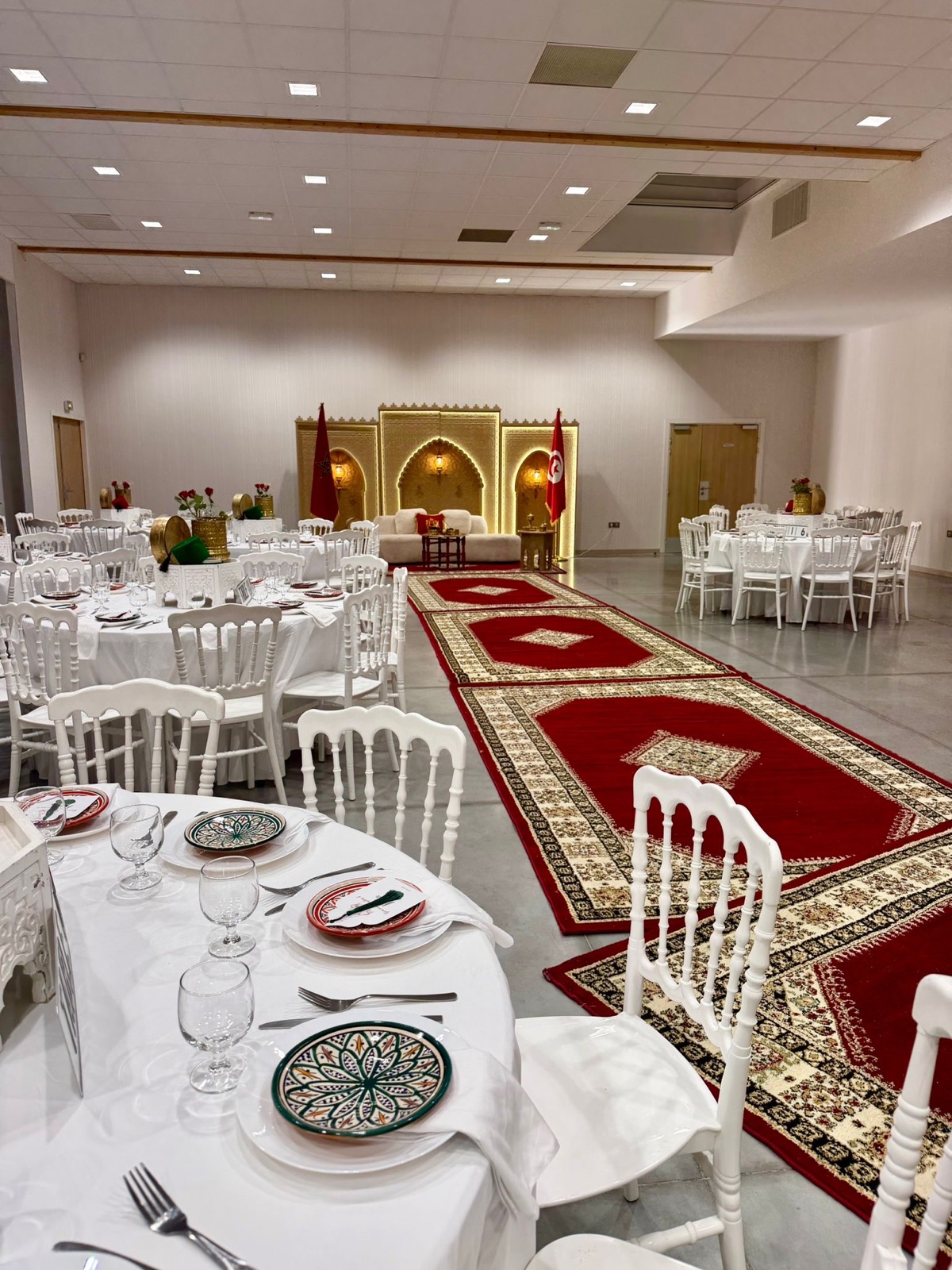 Grande salle d'événement professionnel avec tapis rouge, chaises blanches et fond doré