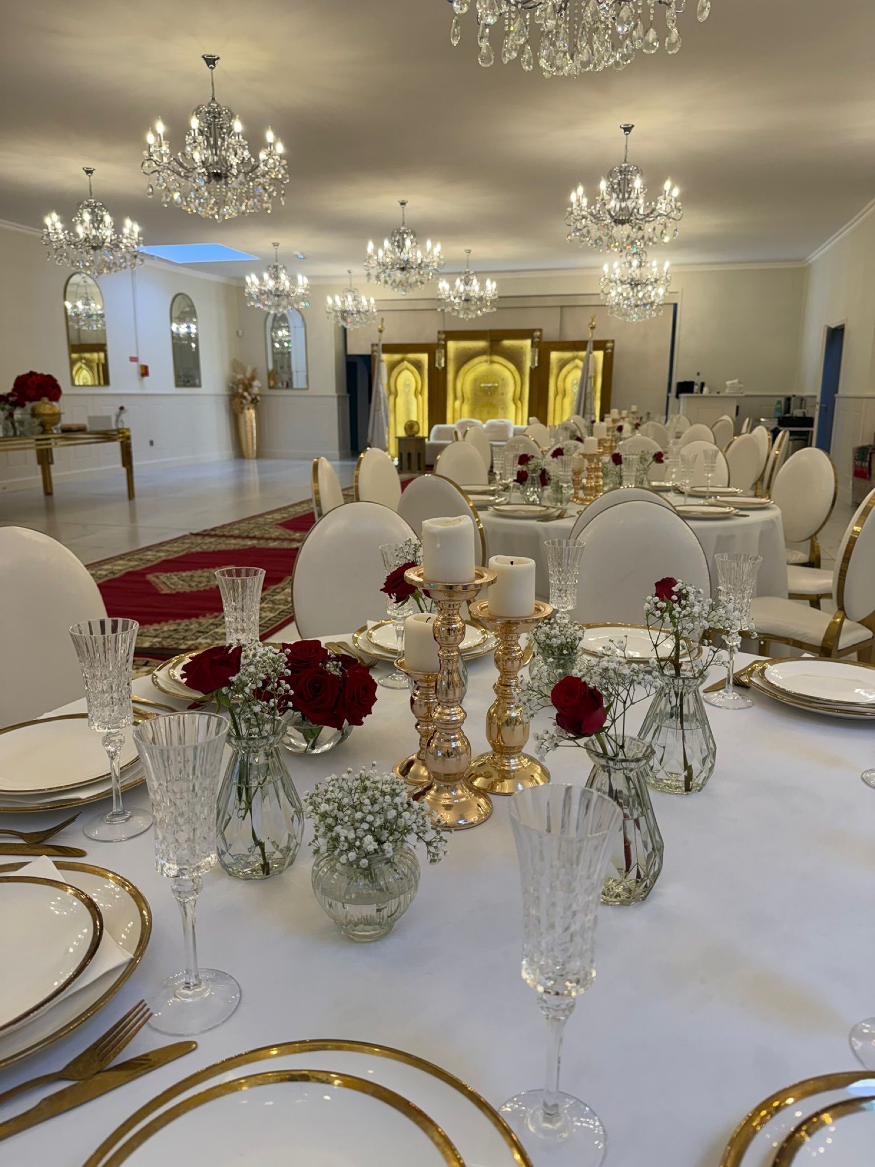 Décoration de table de mariage luxueuse avec lustres en cristal, roses rouges, bougies et vaisselle dorée