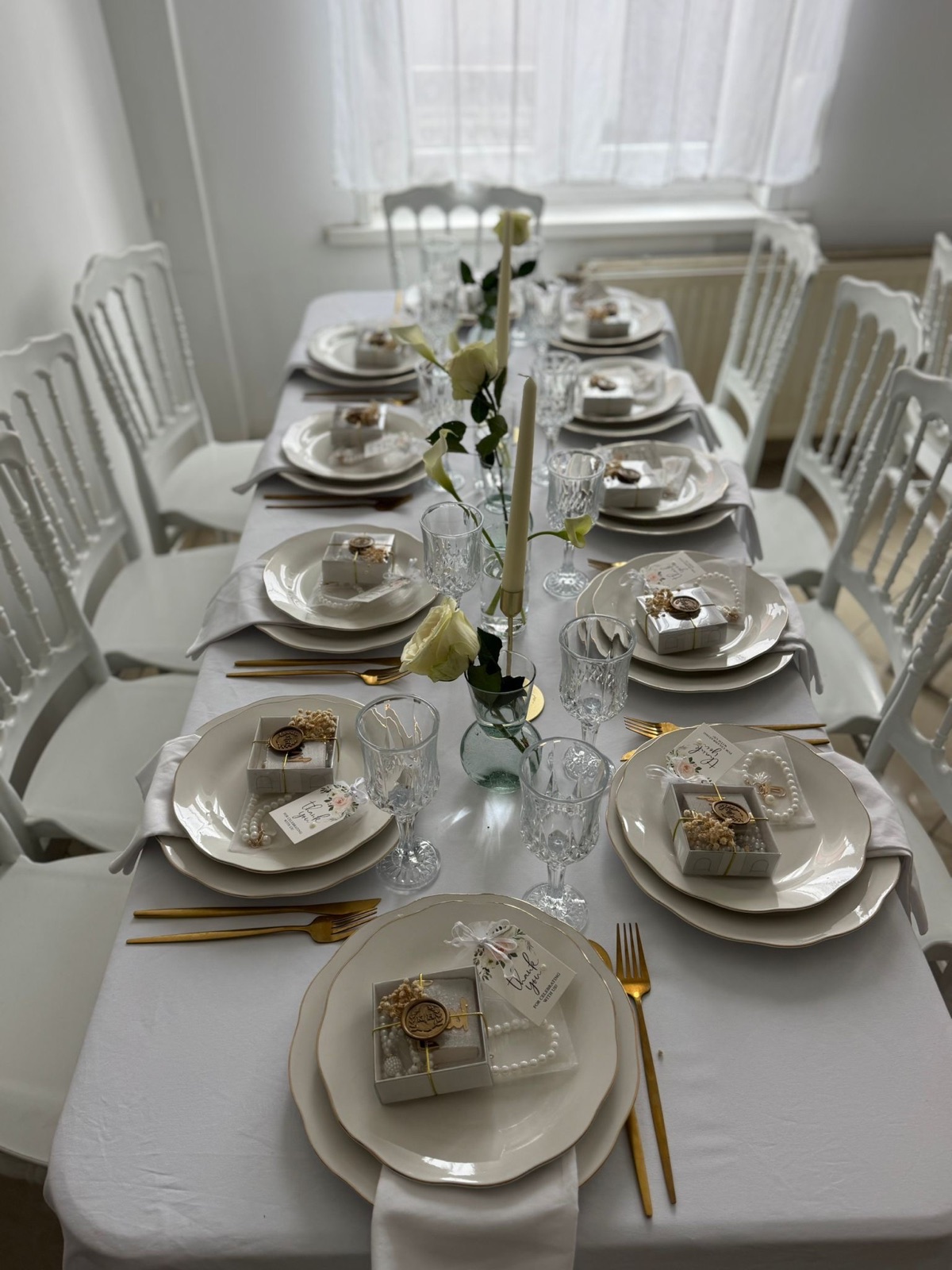 Table blanche intime avec roses, bougies, perles et couverts dorés