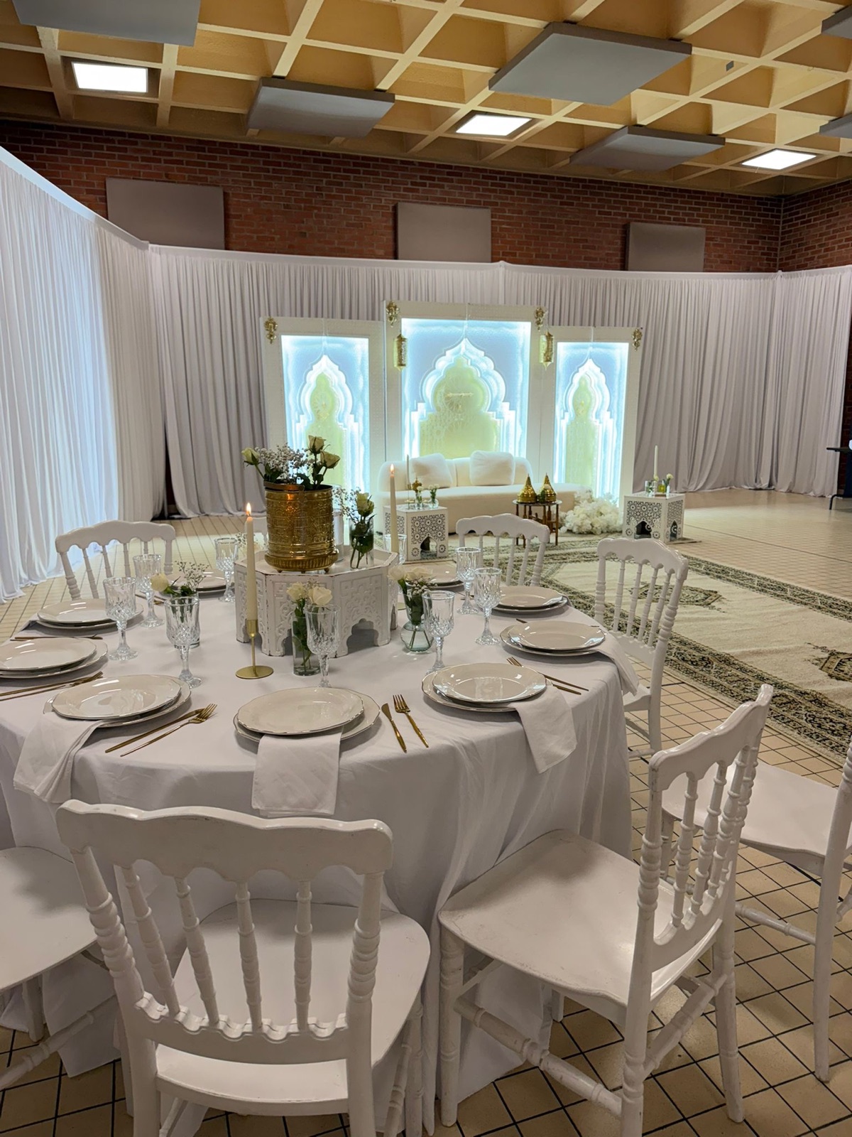 Mise en scène événementielle blanche avec fond lumineux, assise lounge et tables décorées